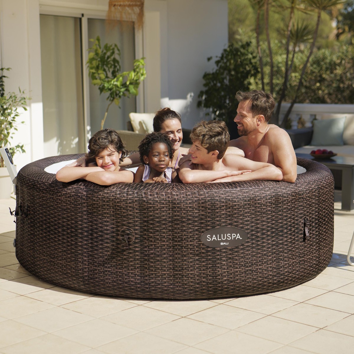 Grupa osób relaksuje się w napełnionym jacuzzi AirJet 7. Produkt znajduje się w ogrodzie na tle nowoczesnej architektury.